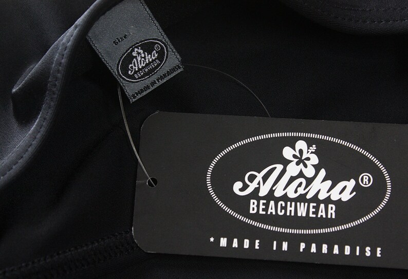 May include: Black and white label with the text "Aloha Beachwear" and a hibiscus flower graphic. The text "Made in Paradise" is below the logo.