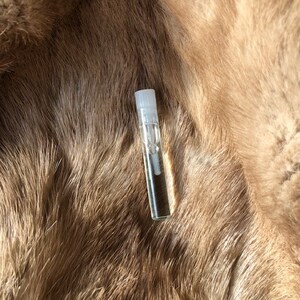 May include: A clear glass bottle with a white cap, filled with a light brown liquid, sitting on a brown fur surface.