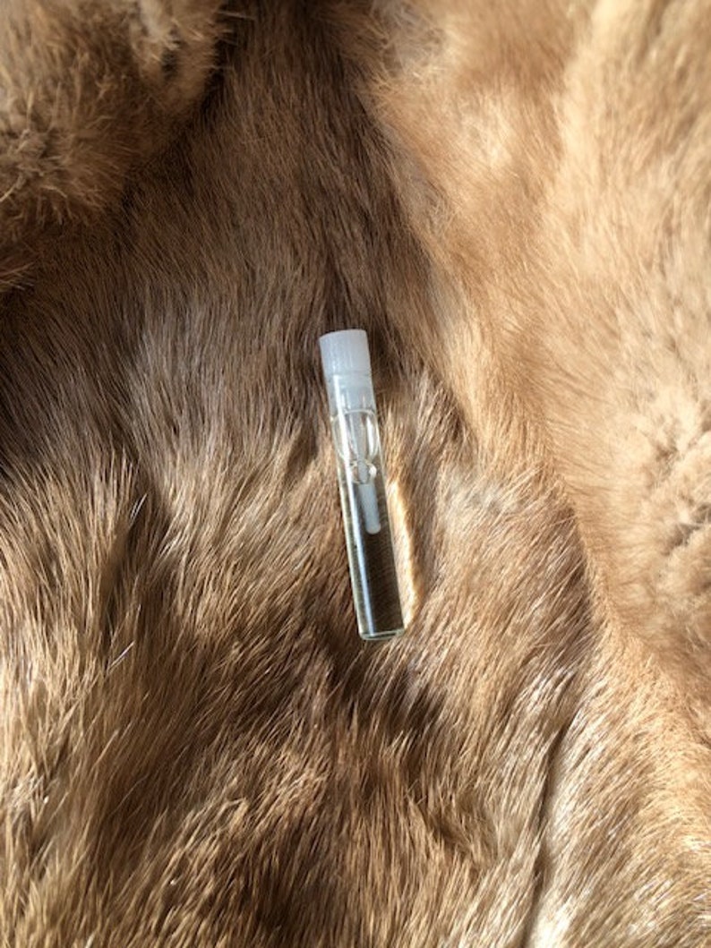 May include: A clear glass bottle with a white cap, filled with a light brown liquid, sitting on a brown fur surface.