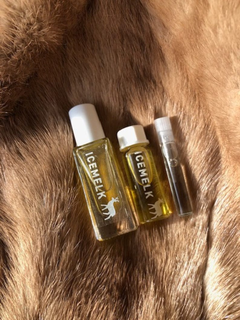 May include: Three glass bottles of perfume with white labels and a deer logo. The labels read "ICEMELK". The bottles are on a brown fur background.