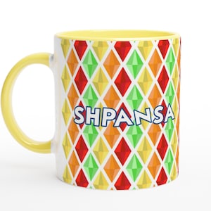 Può includere: Tazza in ceramica bianca con manico e interno gialli. La tazza presenta un colorato motivo a rombi in rosso, verde, arancione e giallo. La parola "SHPANSA" è stampata in blu sulla parte anteriore.