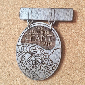 May include: Wooden sign for "The Sleeping Giant Inn" with an engraved design. The oval sign has a rectangular top, connected by metal loops. The design shows a mountain scene and the inn's name. A decorative item.