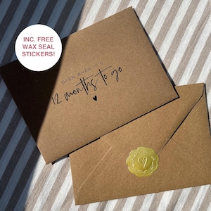 May include: A brown envelope with the text "OPEN WHEN IT'S 12 MONTHS TO GO" and a small heart. The envelope has a gold wax seal sticker with a heart design.