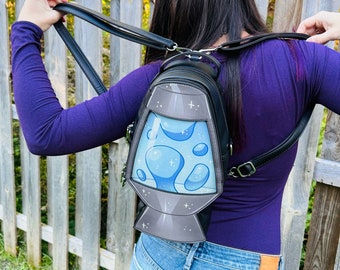 Pode incluir: Uma mochila preta com um design de lava lamp azul e branca. A mochila tem alças ajustáveis e um fecho de correr.