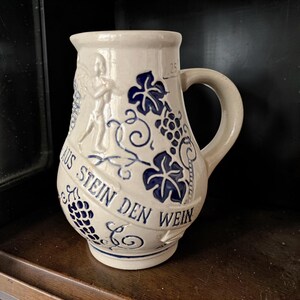 May include: A white ceramic mug with a black handle and the text "But First, Coffee" in a black, handwritten-style font. The mug is on a white surface.