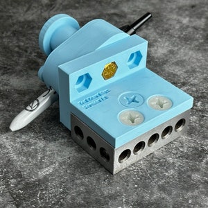 以下が含まれることがあります： 銀色の金属製のベースを持つ、薄い青色の3Dプリントされたツール。ツールには小さな金色のネジと2つの白いネジがあります。ツールの側面には「Remarkable」という文字が印刷されています。