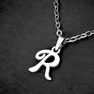 May include: A silver-toned metal necklace featuring a cursive letter R pendant suspended from a delicate cable chain. The pendant has a smooth, polished finish and is attached to the chain by a simple metal bail, creating a classic jewellery piece.