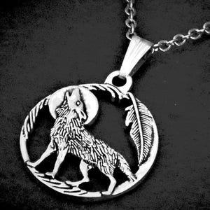 May include: A silver-toned metal pendant necklace featuring a circular frame with a cutout design of a wolf howling at a moon. A single feather is depicted on the right side of the circle. The pendant hangs from a matching silver-toned metal chain.
