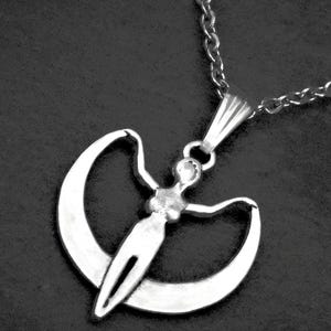 May include: A silver-toned pendant necklace featuring a stylized human figure with outstretched arms positioned in front of a crescent moon shape. The pendant is suspended from a matching silver-toned metal chain link necklace.