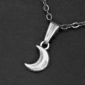 May include: A silver-toned crescent moon pendant suspended from a matching silver-toned metal chain. The pendant features a smooth, polished surface and is attached to the chain by a simple, tapered metal bail, creating a clean and reflective look.