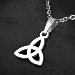 May include: A silver pendant necklace with a Celtic knot design. The pendant, a stylized trefoil, hangs from a fine chain. The necklace is shown against a dark backdrop, emphasizing the intricate details of the jewellery.