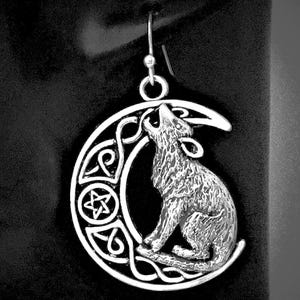 May include: Silver-toned earring featuring a howling wolf silhouette set against a crescent moon. The moon design incorporates Celtic knotwork and a five-pointed star. The earring hangs from a simple hook.