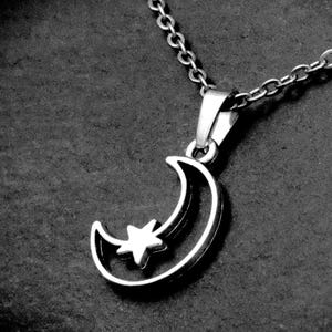 May include: A silver-toned metal pendant necklace featuring a crescent moon shape with a small five-pointed star nestled within the curve. The pendant is attached to a delicate link chain, showcasing a polished metallic finish throughout the design.