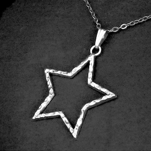 May include: A silver-colored star pendant necklace. The star has a hammered texture and is suspended from a delicate chain. The necklace is displayed against a dark, textured background.