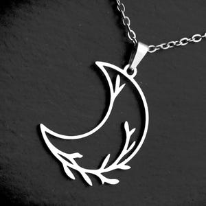 May include: A silver-toned metal necklace featuring a crescent moon pendant. The pendant has a cutout design where one side of the moon is formed by a delicate, branching vine with small leaves. The pendant hangs from a thin, matching silver chain.
