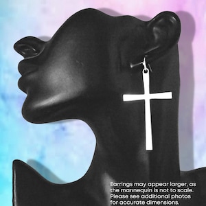 May include: Silver cross dangle earrings. The earrings are shown on a black mannequin head. Earrings may appear larger, as the mannequin is not to scale. Please see additional photos for accurate dimensions.