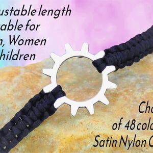 May include: A black satin nylon cord bracelet with a silver gear-shaped centerpiece. The text on the image reads "Adjustable length Suitable for Men, Women & Children" and "Choice of 48 colours Satin Nylon Cord."