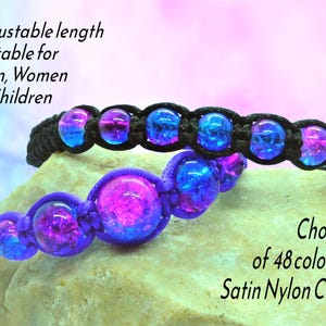 May include: Two macrame bracelets with vibrant, iridescent beads in shades of blue and purple. One bracelet is black, the other is purple. The image includes text that says "Adjustable length" and "Choice of 48 colours".