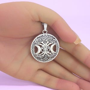 May include: A circular silver-toned pendant featuring an intricate openwork design of a central pentagram flanked by two crescent moons, all set against a detailed background of interwoven Celtic knotwork patterns, suspended from a silver-toned chain.