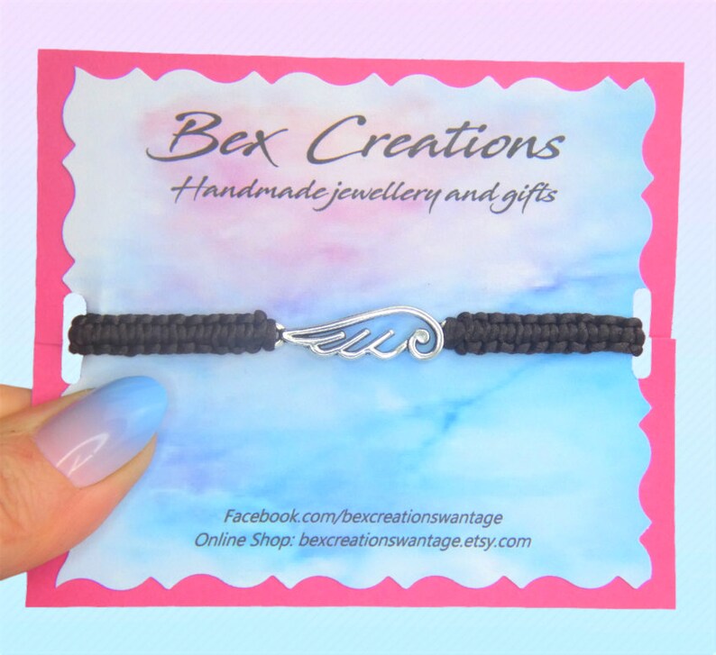May include: A black macrame bracelet with a silver-colored wing charm. The bracelet is displayed on a card with the text "Bex Creations Handmade jewellery and gifts". The card has a pink border and a blue and white watercolor background.