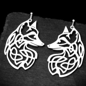 May include: Two silver earrings, each shaped like a fox head with a Celtic knot design. The fox heads are detailed with cut-out patterns. The earrings are suspended from small silver hooks, offering a striking, artistic appearance.
