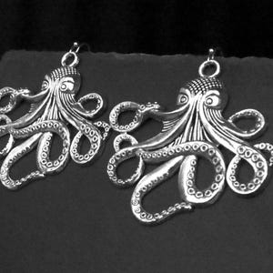 May include: A pair of silver-toned metal octopus earrings featuring detailed tentacles with visible suction cups and textured heads. Each octopus charm is suspended from a simple metal hook, showcasing a metallic finish with dark recessed areas.