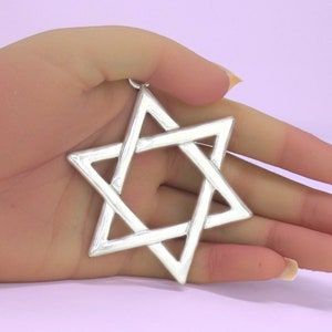 May include: A silver-toned Star of David pendant featuring a six-pointed geometric design with smooth, polished edges. The star is constructed from two interlocking triangles, creating a classic hexagram shape with a small loop at the top.