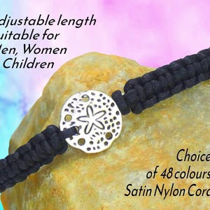May include: A black braided nylon cord bracelet featuring a circular silver-toned sand dollar charm with a central starfish design. The text on the image reads: Adjustable length Suitable for Men, Women & Children and Choice of 48 colours Satin Nylon Cord.