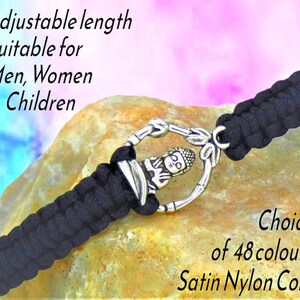 May include: A black braided satin nylon cord bracelet featuring a silver-toned circular charm with a central Buddha figure. The text on the image reads: Adjustable length Suitable for Men, Women & Children and Choice of 48 colours Satin Nylon Cord.