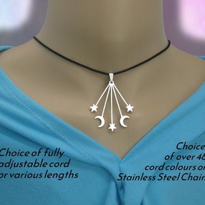 May include: A silver-toned pendant featuring a celestial design with three stars and two crescent moons hanging from thin vertical bars on a black cord. The text reads: Choice of fully adjustable cord or various lengths and Choice of over 48 cord colours or Stainless Steel Chain.