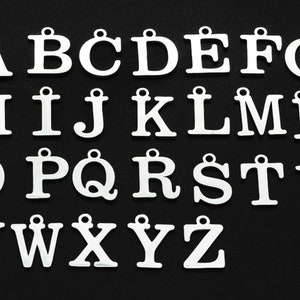 May include: A collection of white metal alphabet letter charms, each with a small loop at the top for attaching to jewelry or other crafts. The letters are displayed against a black background.