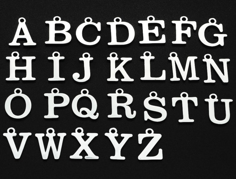 May include: A collection of white metal alphabet letter charms, each with a small loop at the top for attaching to jewelry or other crafts. The letters are displayed against a black background.