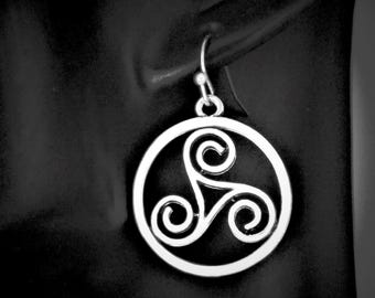 May include: A silver-toned earring featuring a circular frame enclosing a triskelion symbol. The design consists of three interconnected spirals radiating from the center. The earring hangs from a simple hook wire, showcasing a polished metallic finish.