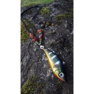 Könnte beinhalten: Eine Halskette mit einem realistisch aussehenden Köderfisch-Anhänger. Die Halskette ist aus schwarzem Band gefertigt und hat rote, grüne und orange Perlen.