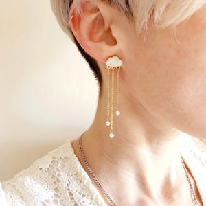 May include: Gold dangle earrings with a white cloud charm and pearl accents.