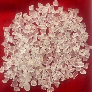 Puede incluir: Un montón grande de cristales de cuarzo transparentes, también conocidos como cristales de roca, sobre un fondo rojo. Los cristales son de varios tamaños y formas, algunos son más redondeados y otros más angulares.