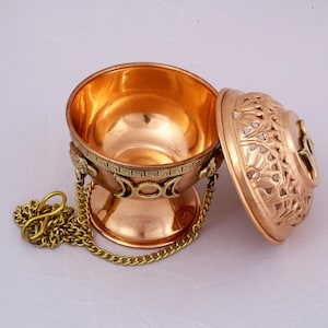 May include: Copper incense burner with a chain and a decorative lid. The lid has a floral design and a triple moon symbol. The burner has a triple moon symbol and a Greek key design.