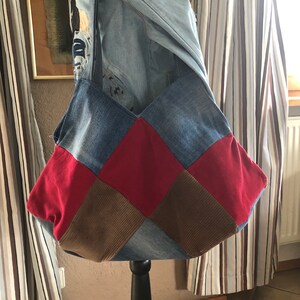 Könnte beinhalten: Eine Patchwork-Tragetasche aus Jeans, rotem Stoff und braunem Cord. Die Tasche hängt an einem schwarzen Ständer.