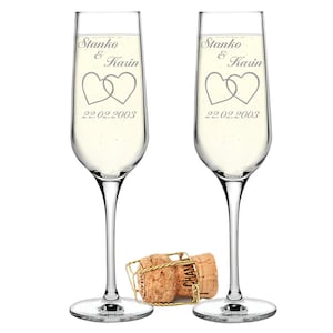 Può includere: Due flute da champagne trasparenti con cuori incisi e il testo "Stanko & Karin 22.02.2003" su ogni bicchiere. Un tappo di champagne è in primo piano.