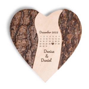 Peut inclure: Une plaque en bois en forme de cœur avec une texture d'écorce. La plaque présente un calendrier pour décembre 2022 avec un cœur marquant le 19. Le texte "Denise & Daniel" est gravé sous le calendrier.