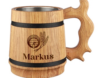 Op de afbeelding: Een houten bierpul met een roestvrijstalen binnenkant. De pul heeft een zwarte band rond de boven- en onderkant, en een ontwerp van een vat met tarwehalmen en de naam "Markus" gegraveerd op de voorkant.