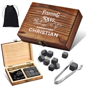Könnte beinhalten: Holzkiste mit einer schwarzen Tasche, einem Satz Whisky-Steinen und einer Zange. Die Kiste ist mit dem Text "Fishing Adventure Christian" graviert.