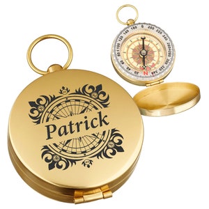 Könnte beinhalten: Ein goldener Kompass mit einer schwarzen Kompassrose und dem Namen "Patrick" auf dem Deckel graviert. Der Kompass hat einen Klappdeckel und eine kleine Schlaufe zum Anbringen einer Kette.