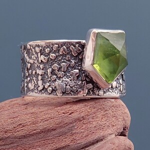 May include: A silver ring with a textured band and a large, faceted, green gemstone.