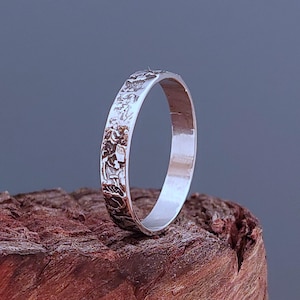May include: A silver band ring with a textured, hammered finish. The ring is simple and elegant, with a smooth interior.