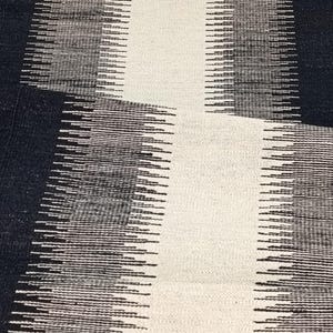 May include: A black and white abstract rug with a geometric pattern. The rug has a textured surface and is made of woven fibers.
