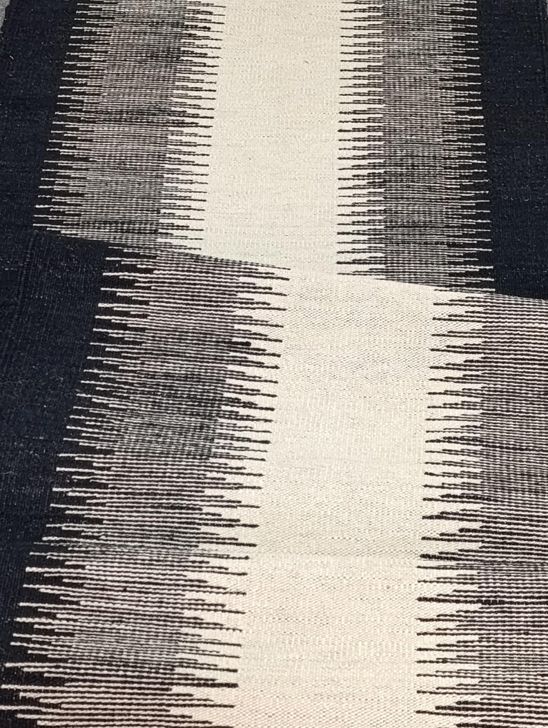 May include: A black and white abstract rug with a geometric pattern. The rug has a textured surface and is made of woven fibers.