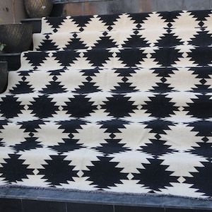 Puede incluir: Alfombra geom&eacute;trica de patr&oacute;n blanco y negro con borde de flecos. La alfombra est&aacute; colocada en un conjunto de escaleras.
