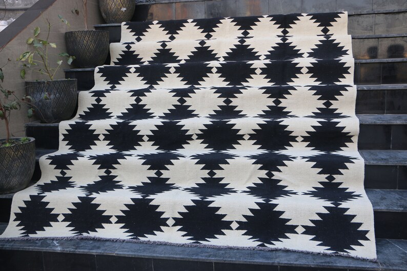Puede incluir: Alfombra geom&eacute;trica de patr&oacute;n blanco y negro con borde de flecos. La alfombra est&aacute; colocada en un conjunto de escaleras.