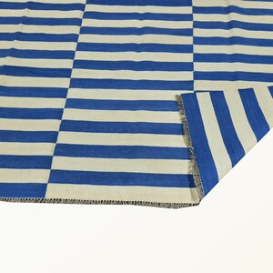 May include: A blue and white striped rug with a woven texture. The rug is folded in half, showing the fringe on the edge.